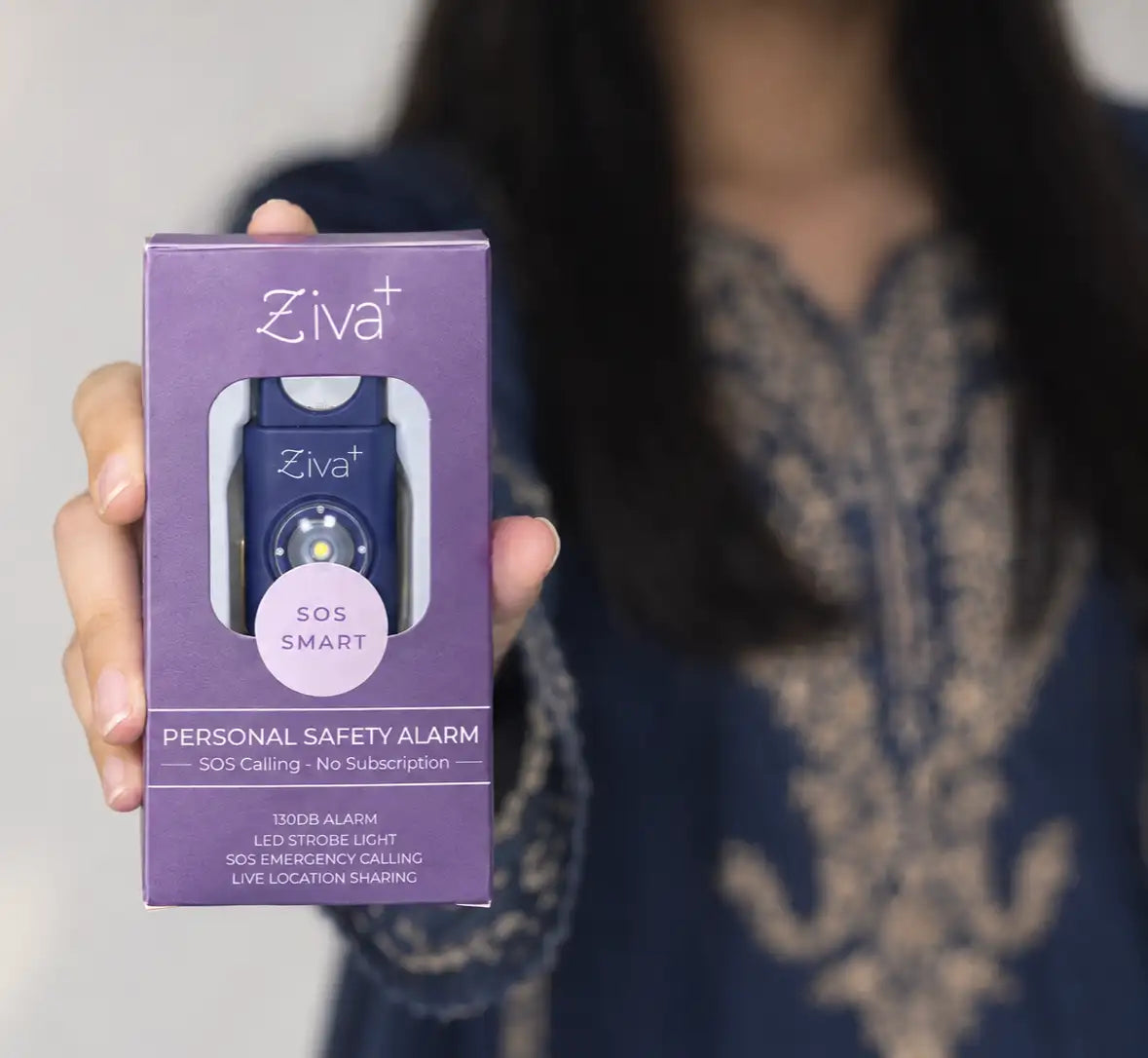 Hand holding the boxed Ziva+ SOS Safety Alarm in navy blue